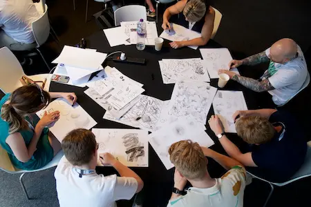 Workshop attendees gathered round a table, engrossed in sketching.