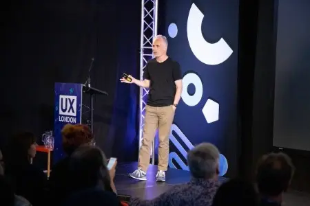 A man speaking on stage, gesturing with one hand.