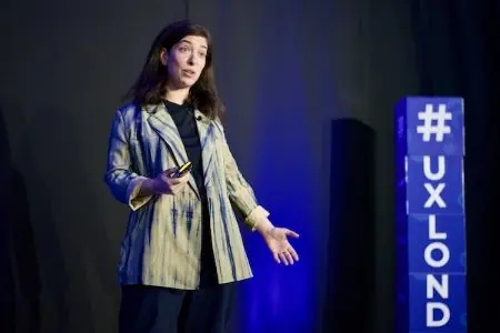 A woman speaking on stage with a clicker in one hand.