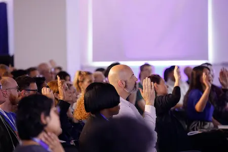 An audience of people raising their hands during a talk.