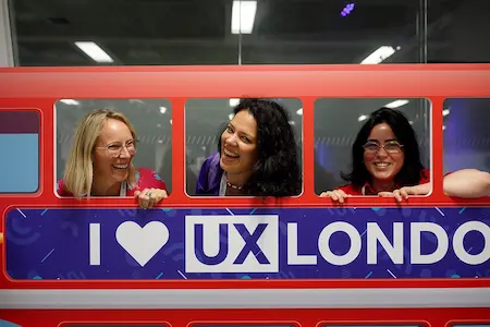 Three laughing women look out of a mockup of a London bus branded for UX London.