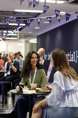 Two women smiling and chatting at a table during a break.